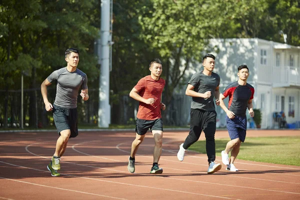 a group of four young asian athletes training on track.