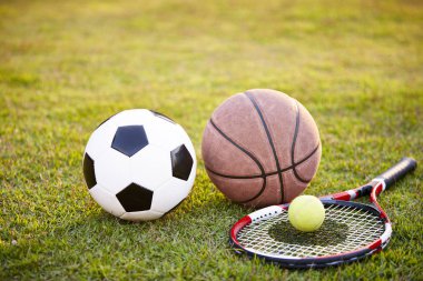 futbol futbol topu basketbol tenis top ve raket çimenlerin üzerinde günbatımında koydu