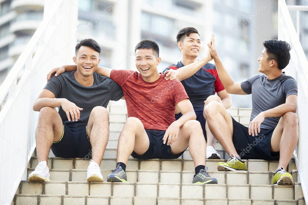 group of four happy young asian male athletes sitting on steps relaxing