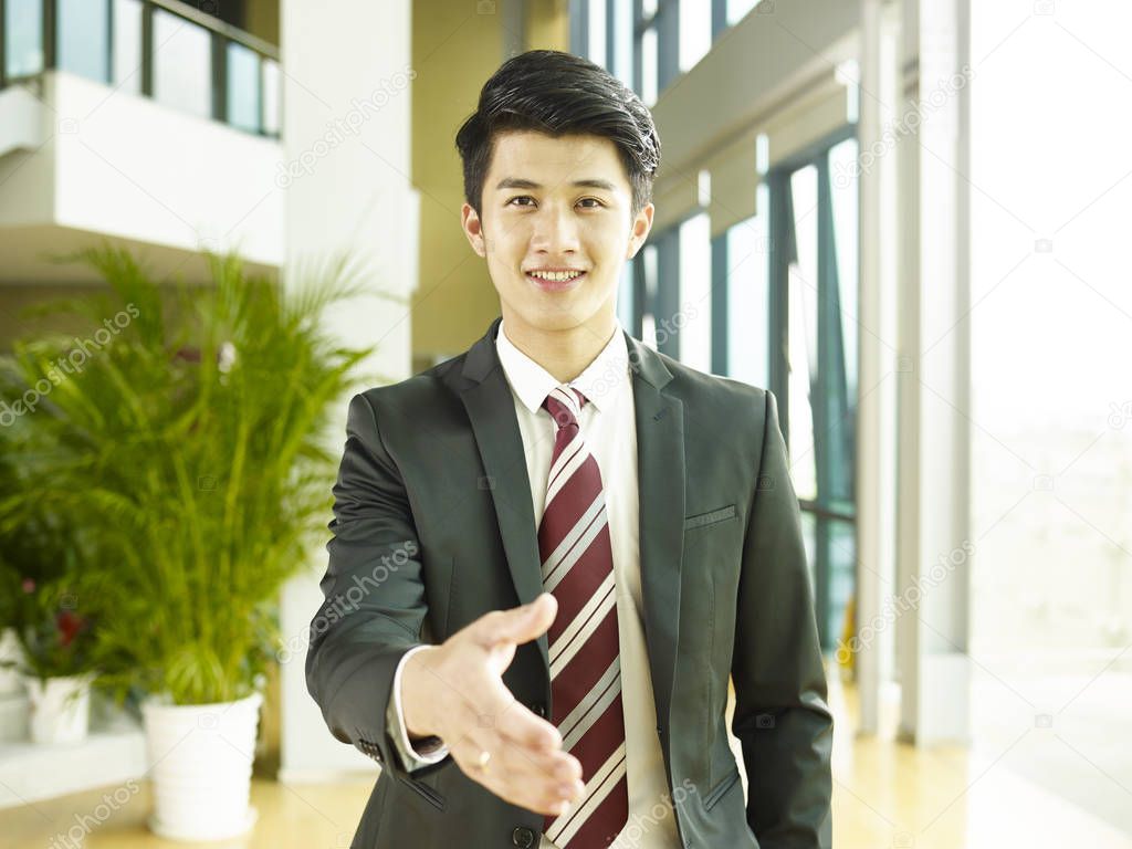 young asian corporate executive reaching out for a handshake, looking at camera smiling.