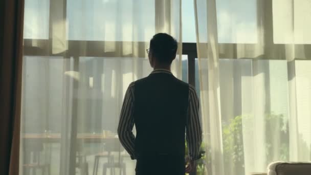 Азиатский Мужчина Открывает Занавески Выходя Балкон Глядя Пейзаж — стоковое видео