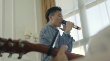 Genç Asyalı erkek şarkıcı şarkı şarkı gitar eşliğinde prova.