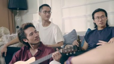 Grup Genç Asya yetişkin adam içki bira şarkı ve evde gitar çalmak toasting toplama