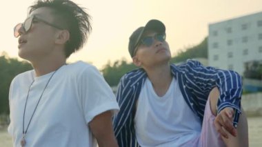 iki genç Asya Yetişkin muscian kumsalda, yavaş hareket rahatlatıcı şarkı oturan.