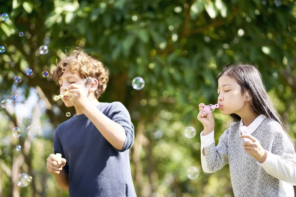 Little Asian Girl Caucasian Boy Playing Together Blowing Soap Bubbles — Stock Photo, Image