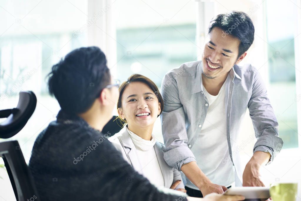 three happy asian teammates discussing business in office