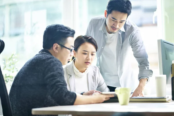 Tres jóvenes empresarios asiáticos discutiendo negocios en oficina —  Fotos de Stock