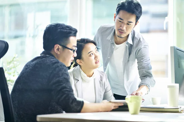 Tres jóvenes empresarios asiáticos discutiendo negocios en oficina —  Fotos de Stock