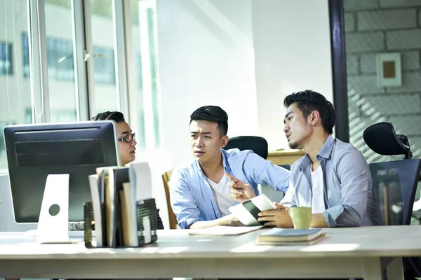 Trzech młodych azjatyckich przedsiębiorców omawia biznes w biurze — Zdjęcie stockowe