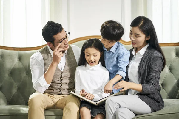 Asiatische Eltern und zwei Kinder lesen gemeinsam Buch — Stockfoto