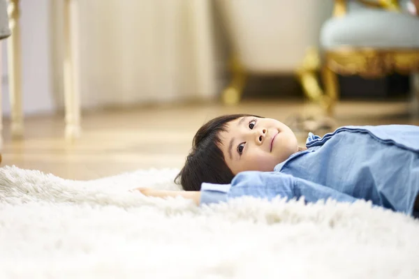 Pequeño asiático chico acostado en espalda en alfombra —  Fotos de Stock