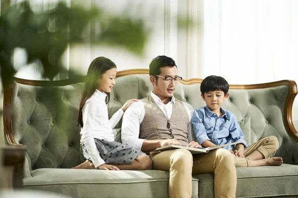 Отец-азиат и двое детей вместе читают книгу — стоковое фото