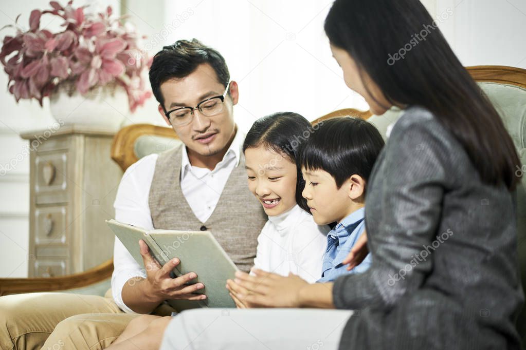 asian mother and father and two children reading book together