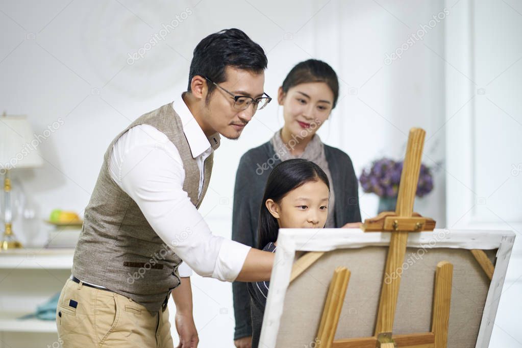 little asian girl making a painting with parents watching and he