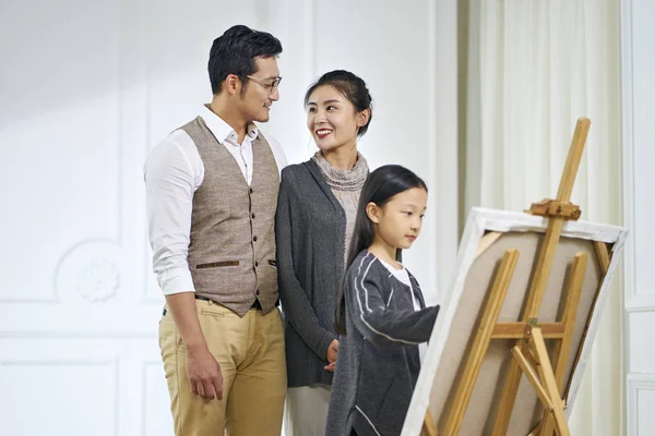 Маленькая азиатская девочка делает картину с родителями, смотрящими — стоковое фото