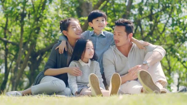 2人の子供を持つアジアの家族は 公園でおしゃべりをしながら屋外の草の上に座っています — ストック動画