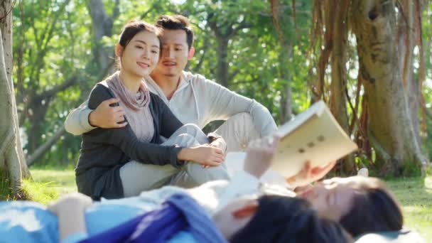 Asian Parents Watching Two Children Lying Grass Reading Book Together — Stock Video