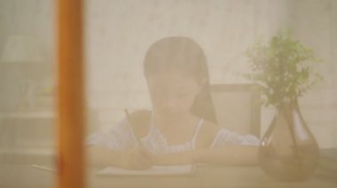 pencere nin önünde oturan uzun siyah saçlı dokuz yıllık küçük asyalı kız yazma veya resim çizim