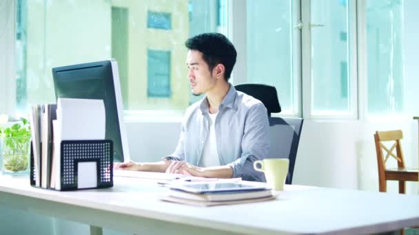 デスクトップコンピュータを使用してオフィスで働く若いアジア人ビジネスマン — ストック動画