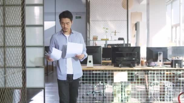 中小企業のオフィスを歩きながら販売レポートを見ているアジアの若いビジネスマン — ストック動画