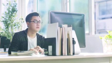 masaüstü bilgisayarda çalışan masada oturan genç asyalı iş adamı