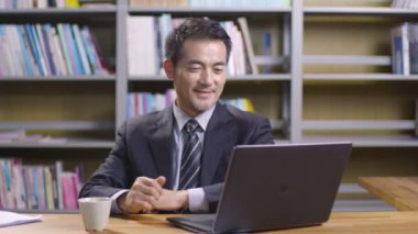 Asyalı üst düzey şirket yöneticisi dizüstü bilgisayar kullanarak ofiste çalışıyor.. 