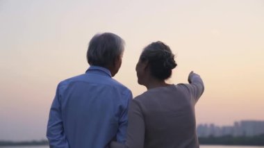 Sevgili Asyalı yaşlı çiftin nehir kenarında durup gün batımını izlediği arka manzara.