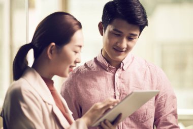 Asyalı iş adamı ve kadın ofiste buluşup dijital tablet kullanarak tartışıyorlar.