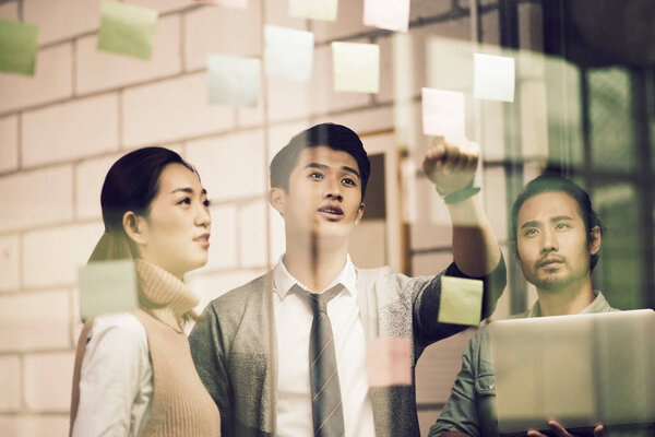 three asian small company businesspeople young entrepreneurs meeing discussing in office using sticky notes