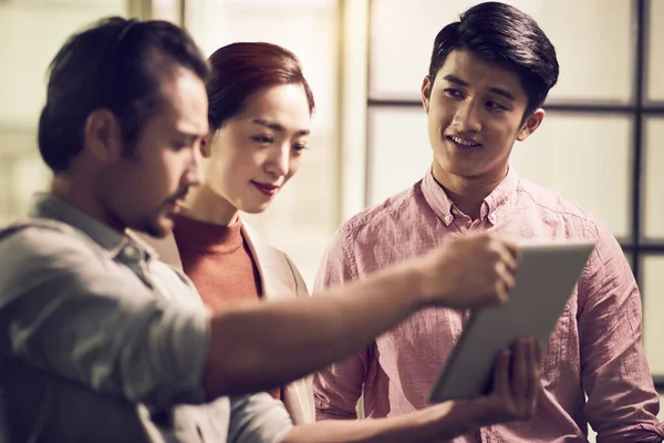 Trzech Młodych Azjatyckich Przedsiębiorców Pracujących Razem Biurze Patrzących Tablety Cyfrowe — Zdjęcie stockowe