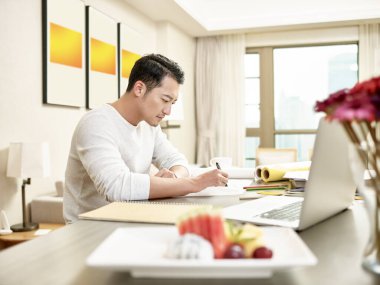 Genç Asyalı tasarım uzmanı mutfak tezgahında oturmuş bir çizime bakıyor (dijital olarak değiştirilmiş arkaplanda çizimler))