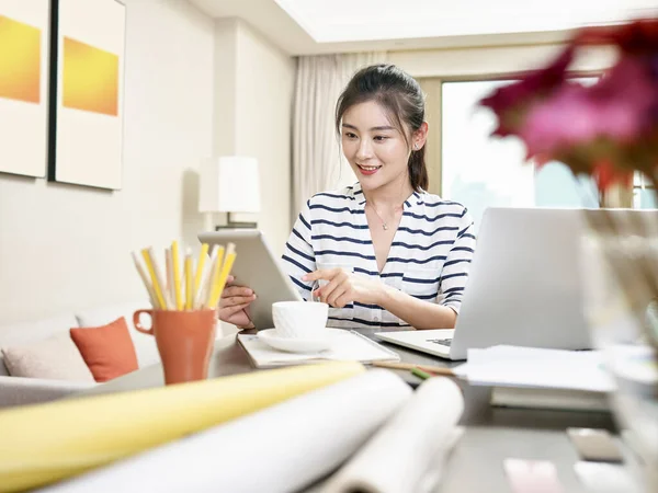 家庭でノートパソコンやデジタルタブレットを使って仕事をしている若いアジア人のビジネス女性 背景のアートワークはデジタル的に変化しました — ストック写真