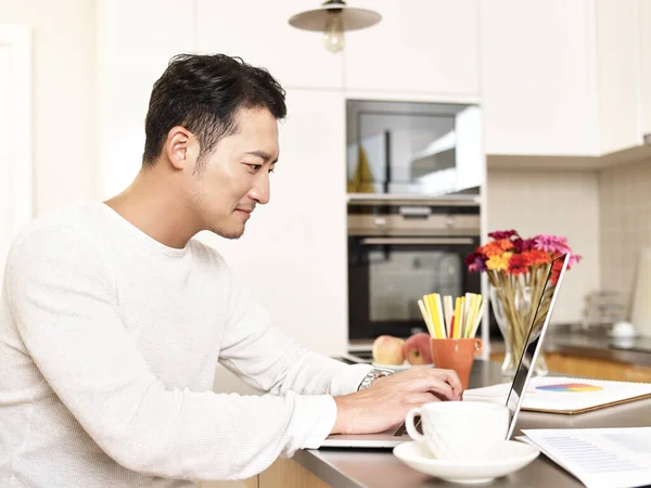 年轻的亚洲商人在家里工作 他坐在厨房的柜台上 使用笔记本电脑 — 图库照片