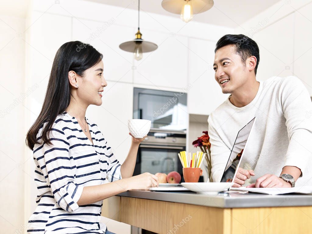 young asian couple working from home sitting kitchen counter having a discussion