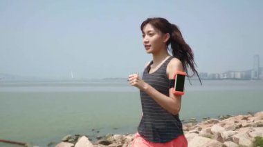 Genç Asyalı kadın deniz kenarındaki parkta koşuyor.