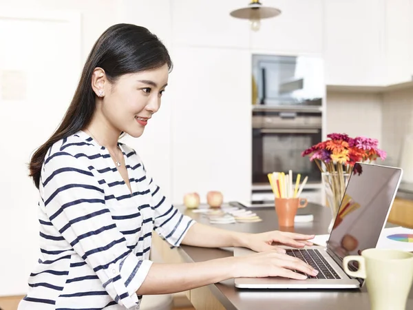 自宅のキッチンカウンターでノートパソコンを使って仕事をしている若いアジア人のビジネスマンが — ストック写真