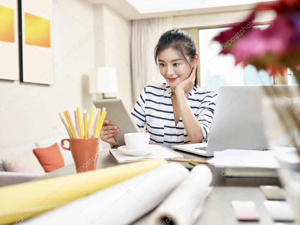 young asian business woman working at home using laptop computer and digital tablet (artwork in background digitally altered)