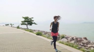 Genç Asyalı kız deniz kenarında bir parkta koşuyor.