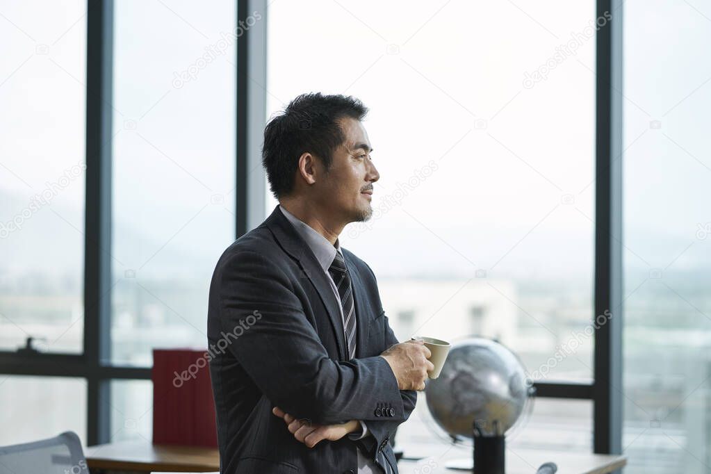 asian corporate executive thinking in office with a cup of coffee in hand, side view