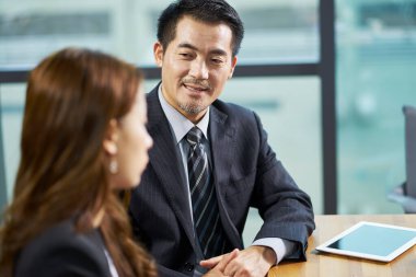 İki Asyalı şirket yöneticisi ofiste sohbet ediyorlar.