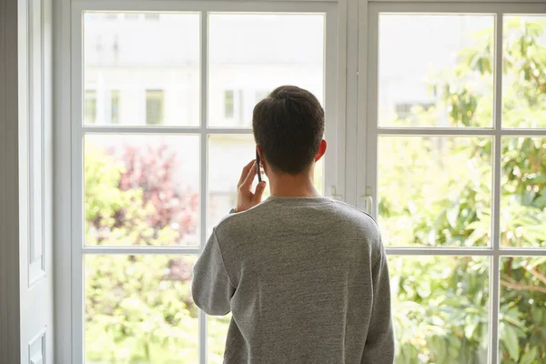 Bakre Ung Asiatisk Man Tittar Genom Fönstret När Pratar Mobiltelefon — Stockfoto