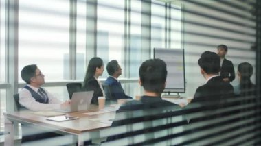 Genç Asyalı yönetici modern ofis konferans odasında personel toplantısında iş planını ekibe sunuyor.