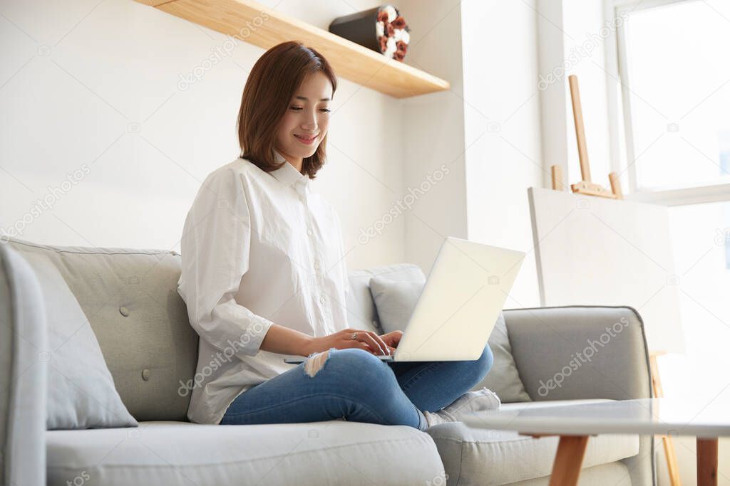 young asian business woman working at home sitting on couch using laptop computer