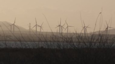 Gün batımında bulutlu bir öğleden sonra rüzgar türbinleri döner hareket.