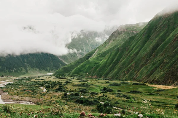 Scenic view of green valley with mountains and cloudy sky in Gergeti, Georgia