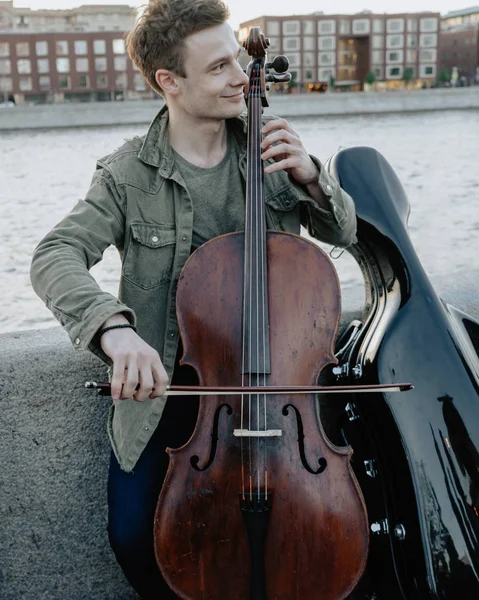 Street musician, young man playing cello in the street of big city, close up, Moscow, Russia