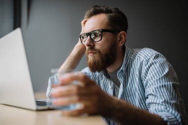 İşyerinde oturan genç iş adamı. Sakallı dizüstü bilgisayar kullanarak, araştırma hipster ve loft Office online bilgileri analiz. Beyin fırtınası. Freelancer planlama proje, son tarih. 