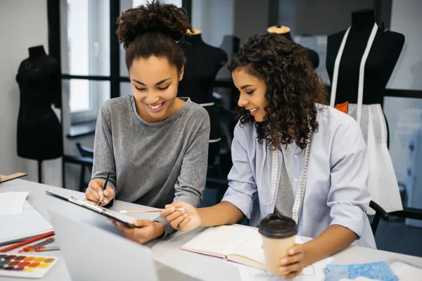 Çizim veya çizim birlikte modern atelier Afro-Amerikan moda ressamlar gülümseyerek. Pozitif kıvırcık saçlı hipsters kadınlar tartışma proje, planlama, strateji birlikte işyerinde boyama. 