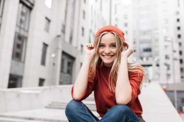 Güzel yüzlü ve gülümseyen neşeli İskandinav kadın portresi. Rengârenk kıyafetler giyen, fotoğraf için poz veren pozitif hipster kırmızı şapka takıyor.