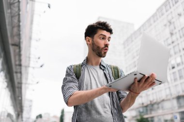 Genç sakallı blogger hayran yüz, şık saç kesimi video akışı ile dizüstü bilgisayar ve ücretsiz internet bağlantısı şehrin sokak kullanma online. Yakışıklı adam alışveriş online, indirimli satış.